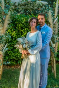 Photographe de mariage 04 - Couple de mariés enlacés devant une arche fleurie, la mariée tient son bouquet en Alpes-de-Haute-Provence