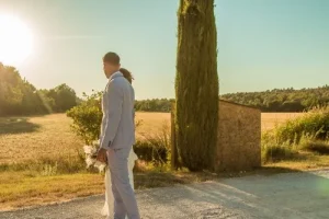 Photographe mariage Vaucluse - Couple de mariés s'avançant devant un cyprès au coucher du soleil dans un champ