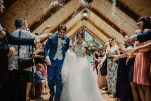 Capture spontanée et joyeuse du lancer de riz sur les mariés à la sortie d'une chapelle en bois, par photographe de mariage professionnel à Digne-les-Bains.