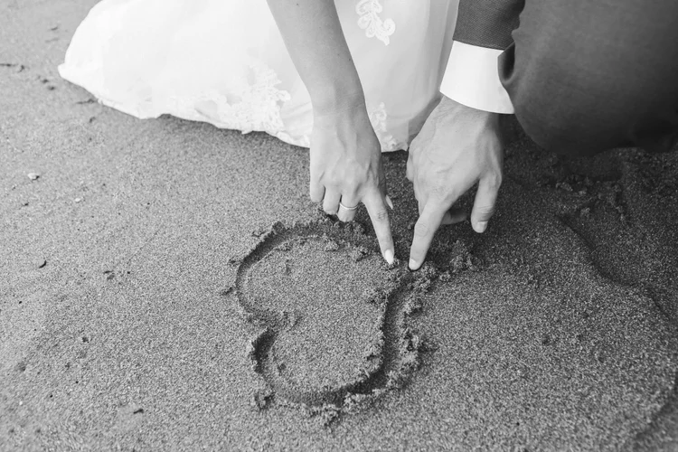 Photographe mariage - Couple de mariés dessinant un cœur sur le sable à la plage