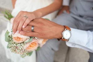 Photographie Fine Art de détails de mariage à Gap : deux alliances en argent posées délicatement sur un bouquet de mariée en fleurs séchées et stabilisées de couleur rose poudré et blanc. Capture élégante par photographe professionnel.