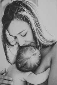 Photo en noir et blanc léger ou maman tient son enfant nouveau né dans ses bras en lui embrassant la tete