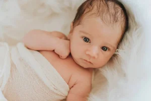 bébé dans un lit, emmailloté dans un linge blanc regarde le photographe professionnel qui va lui faire un shooting dans les alpes de haute provence