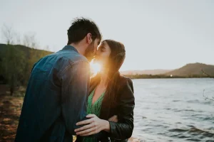 jeune couple qui va s'embrasser devant la mer sur un coucher de soleil qui passe entre leurs levres