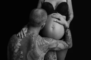 papa est a genoux face a sa femme sur le coté et papa pose sa tete et son bras sur le ventre enceinte de sa femme