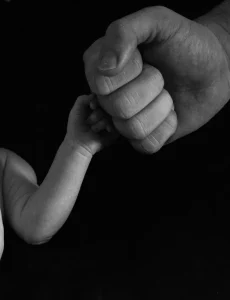 Sur un fond très noir papa fait un check avec le poing de son fils après quelques jours de vie