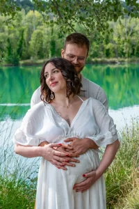 couple amoureux qui se tient fort devant un lac en provence - papa tient le ventre de maman - maman maintient le ventre ou bébé se trouve pour le proteger