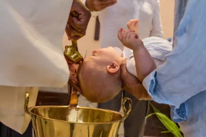 Bébé qui se fait baptiser dans une église par le pretre qui lui verse de l'eau bénite sur le front