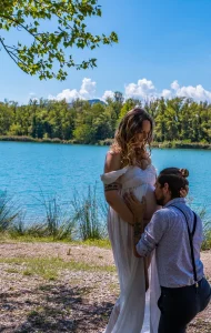 Papa qui embrasse le ventre de maman qui attends un heureux évènement devant un lac bleutée sur la commune des Mées en région paca