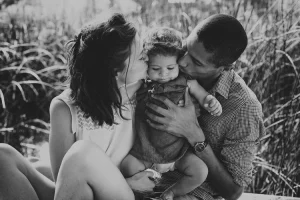 Famille en noir et blanc embrassant leurs enfant dans une prairie